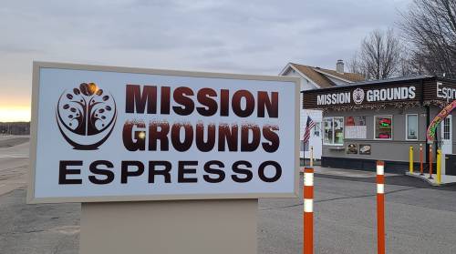 Sign for "Mission Grounds Espresso" with a coffee shop in the background, featuring a cloudy sky.