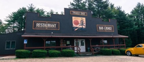 A rustic building with signs for "Trails End Restaurant" and "Bar-Lounge," surrounded by trees and a gravel parking area.