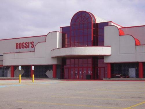Exterior of a closed store named "Rossi's," featuring a large entrance and red accents against a cloudy sky.