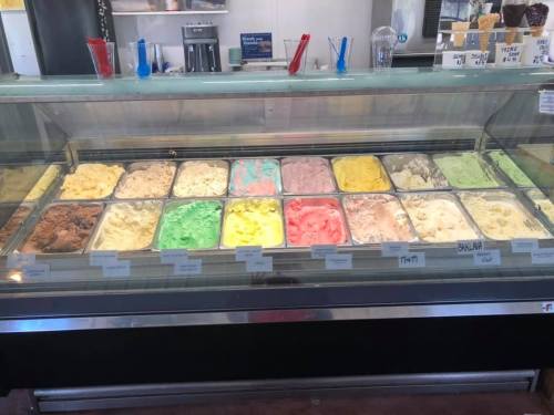 A display case filled with various colorful ice cream flavors in metal tubs, labeled with names.