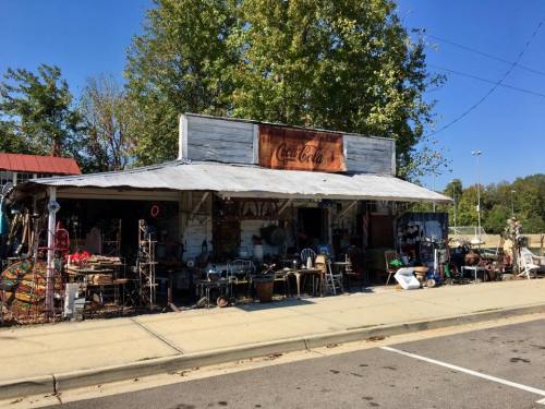A vintage shop with a Coca-Cola sign, filled with various antiques and items, set against a clear blue sky.