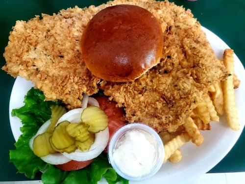 A plate featuring a large fried chicken sandwich, lettuce, tomato, pickles, and crinkle-cut fries.