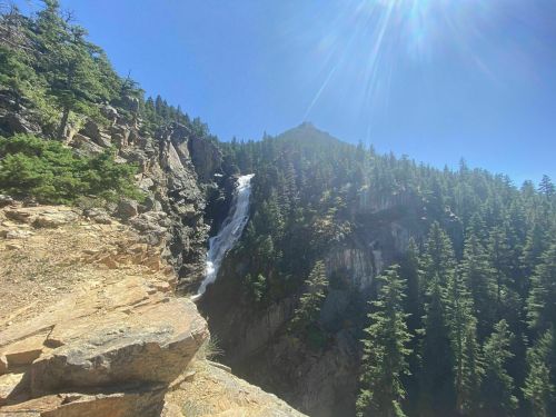 A scenic view of a waterfall cascading down rocky cliffs, surrounded by lush green trees and a clear blue sky.