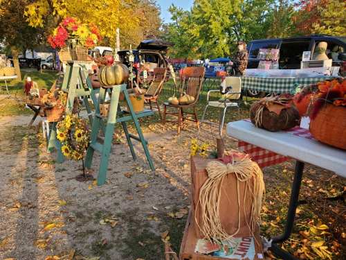 A fall-themed market scene with decorated chairs, pumpkins, and autumn leaves in a vibrant outdoor setting.
