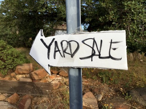A hand-drawn sign on a pole pointing left, labeled "YARD SALE" in bold black letters.