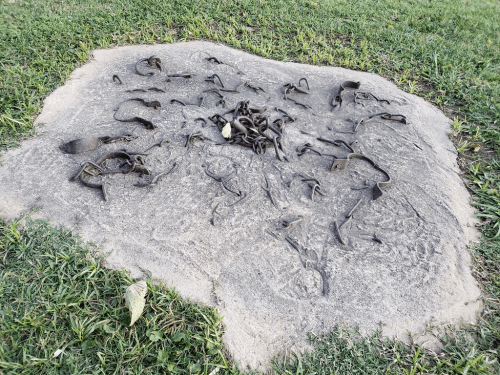 A stone slab with various rusted metal pieces scattered across its surface, surrounded by green grass.
