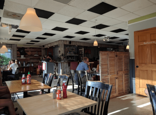 Interior of a casual restaurant with wooden decor, tables, and patrons dining. Ketchup bottles are on the tables.