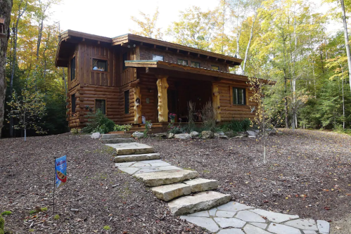 A rustic log cabin surrounded by trees, featuring a stone pathway leading to the entrance.