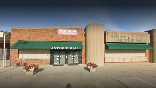 Exterior of an antique mall with a "Now Open Sunday" sign, featuring green awnings and flower planters.