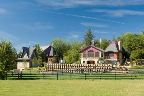 A picturesque countryside scene featuring colorful houses and stacked logs, surrounded by lush greenery and blue skies.