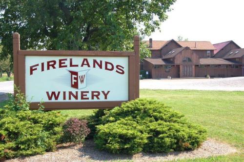 Sign for Firelands Winery with a rustic building in the background and green landscaping.