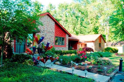 A charming brick house surrounded by lush greenery and colorful flowers, featuring a decorative garden sculpture.