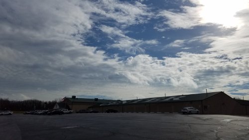 A large building with the word "CENTER" on its side, under a cloudy sky with the sun peeking through. Cars are parked nearby.