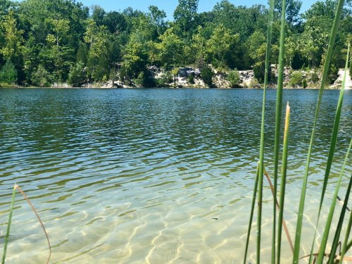 A serene lake surrounded by lush greenery and rocky cliffs, with clear water reflecting the blue sky.