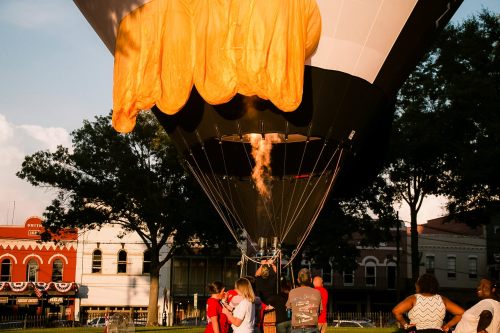 A hot air balloon being prepared for flight, with people gathered around in a park during sunset.