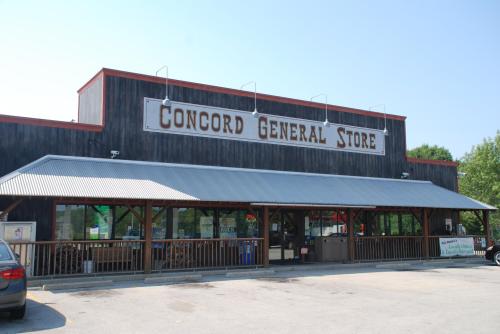 Exterior of Concord General Store, featuring a wooden facade, large sign, and a covered porch with windows.