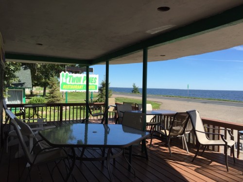 View from a porch with tables and chairs overlooking a lake and a sign for Twin Pines Restaurant and Hotel.