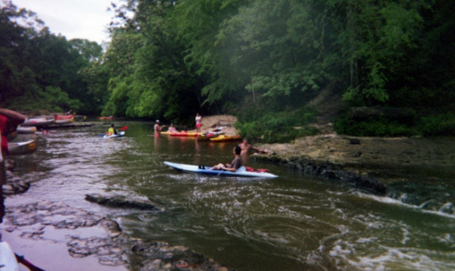 A group of people kayaking on a river surrounded by lush greenery and rocky banks.