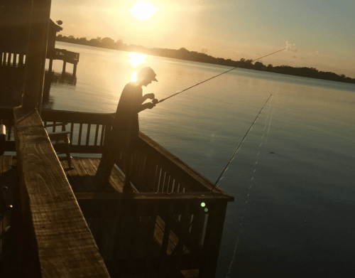 A person fishing from a wooden dock at sunset, with calm water reflecting the golden light.
