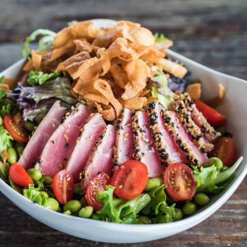 A vibrant salad with sliced seared tuna, cherry tomatoes, greens, and crispy onions in a white bowl.