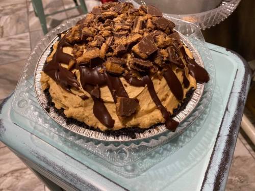 A delicious pie topped with chocolate drizzle and crushed peanut butter cups on a cookie crust.