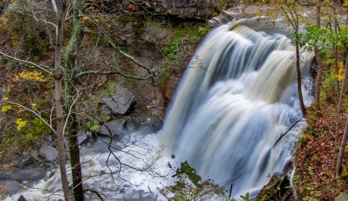 A cascading waterfall surrounded by rocky terrain and autumn foliage, creating a serene natural scene.