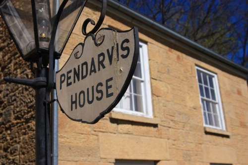 Sign for Pendarvis House in front of a stone building with windows and a clear blue sky.