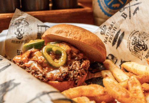 A close-up of a juicy burger topped with cheese and jalapeños, served with crispy fries on a paper-lined plate.