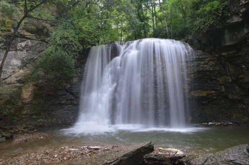 A serene waterfall cascading over rocky cliffs, surrounded by lush green trees and a tranquil pool below.