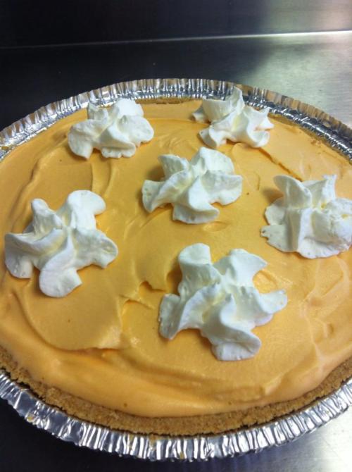 A creamy orange pie topped with dollops of whipped cream in a silver pie crust.