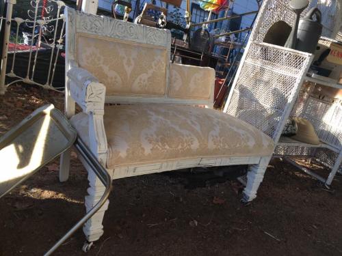 A vintage white settee with ornate carvings and a patterned fabric seat, placed outdoors among various items.