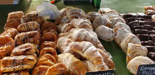 A variety of baked goods wrapped in plastic, including cinnamon rolls and almond pastries, displayed at a market.