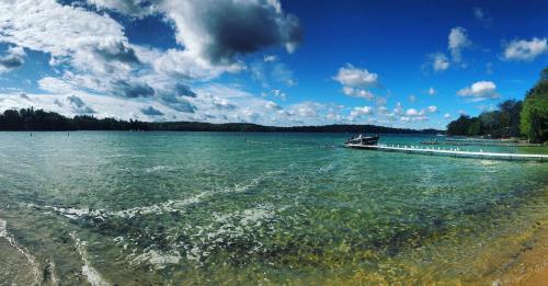 A serene lake scene with clear water, a wooden dock, and a blue sky filled with fluffy clouds.