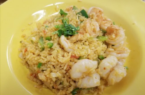 A yellow plate filled with shrimp fried rice, garnished with green onions and cilantro.