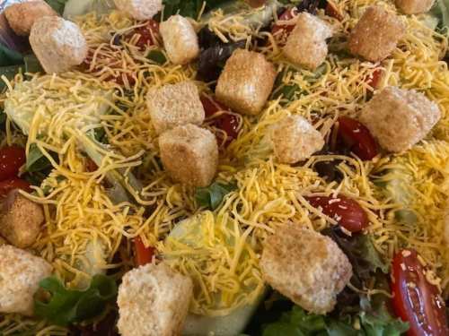 A colorful salad topped with shredded cheese, croutons, cherry tomatoes, and mixed greens.