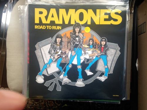 Album cover for "Road to Ruin" by the Ramones, featuring cartoon-style band members with guitars and a city backdrop.