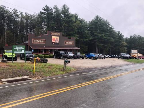 A restaurant and bar with several parked SUVs in front, surrounded by trees on a rainy day.
