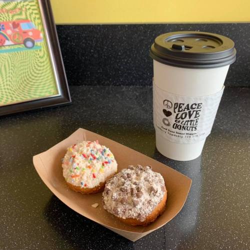 A paper tray holds two donuts, one with sprinkles and the other with chocolate crumbs, beside a coffee cup.