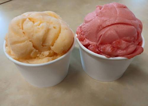 Two cups of ice cream: one peach-colored and one pink, both with a smooth, creamy texture.