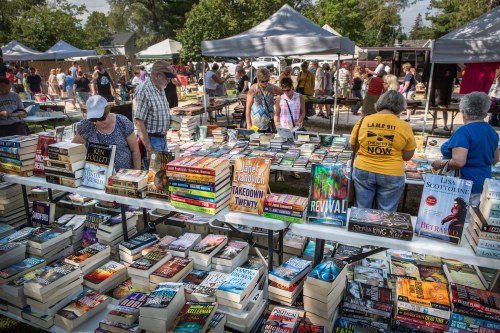 A bustling outdoor book fair with tables filled with books and people browsing under tents.