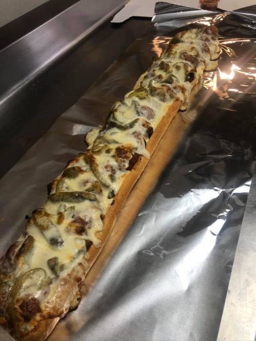 A long sandwich topped with melted cheese and green peppers, resting on aluminum foil.
