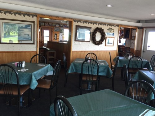 A cozy restaurant interior with green tables, black chairs, and framed pictures on the walls.