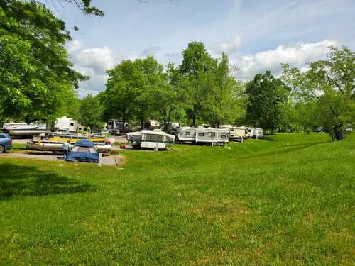 A grassy area with several parked RVs and boats under a blue sky with scattered clouds.