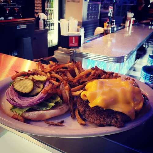 A juicy cheeseburger topped with melted cheese, pickles, and onions, served with a side of crispy fries.