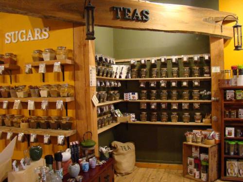 A cozy shop interior featuring shelves of various teas and sugars, with jars and bags neatly organized.