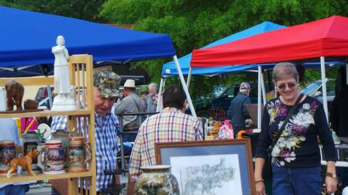 A bustling outdoor market with colorful tents, people browsing antiques, and various items for sale.