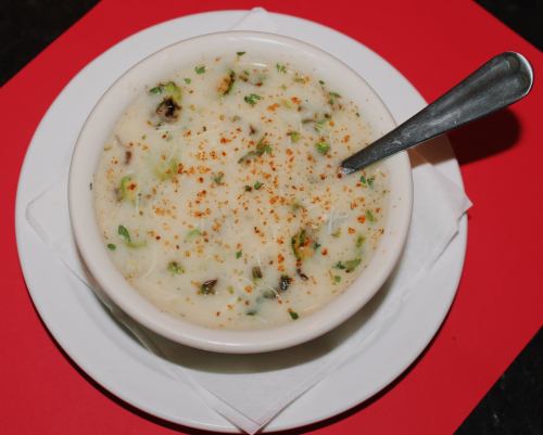A bowl of creamy soup garnished with herbs and spices, served on a white plate with a spoon.