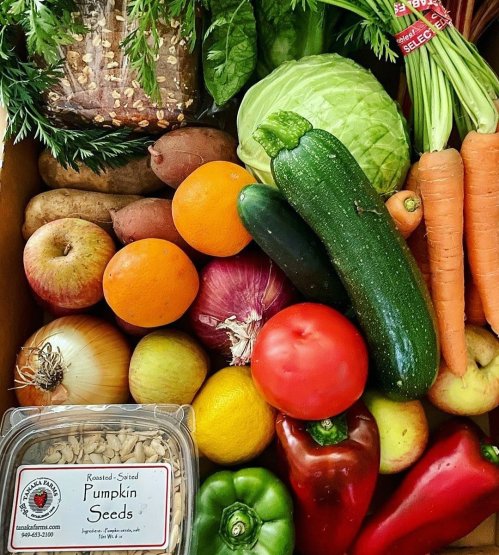 A colorful assortment of fresh vegetables and fruits, including carrots, zucchini, apples, and a container of pumpkin seeds.