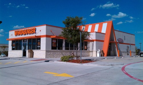 A Whataburger restaurant with orange and white stripes, surrounded by a clear blue sky and a few clouds.