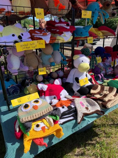 A colorful display of crocheted hats and stuffed animals for sale at a market, with price tags visible.